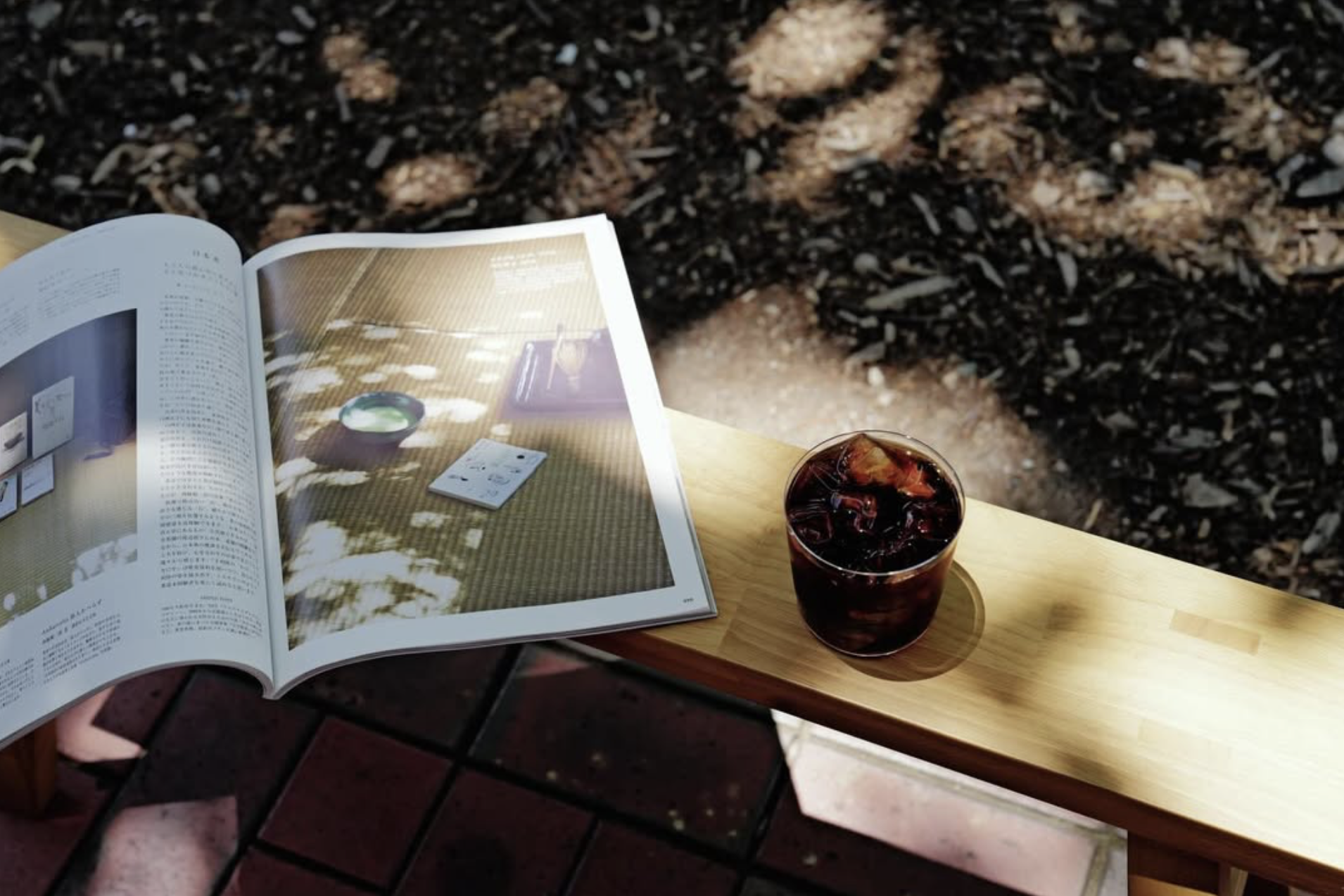 Japanese magazine and iced coffee on a wooden bench in dappled sunlight